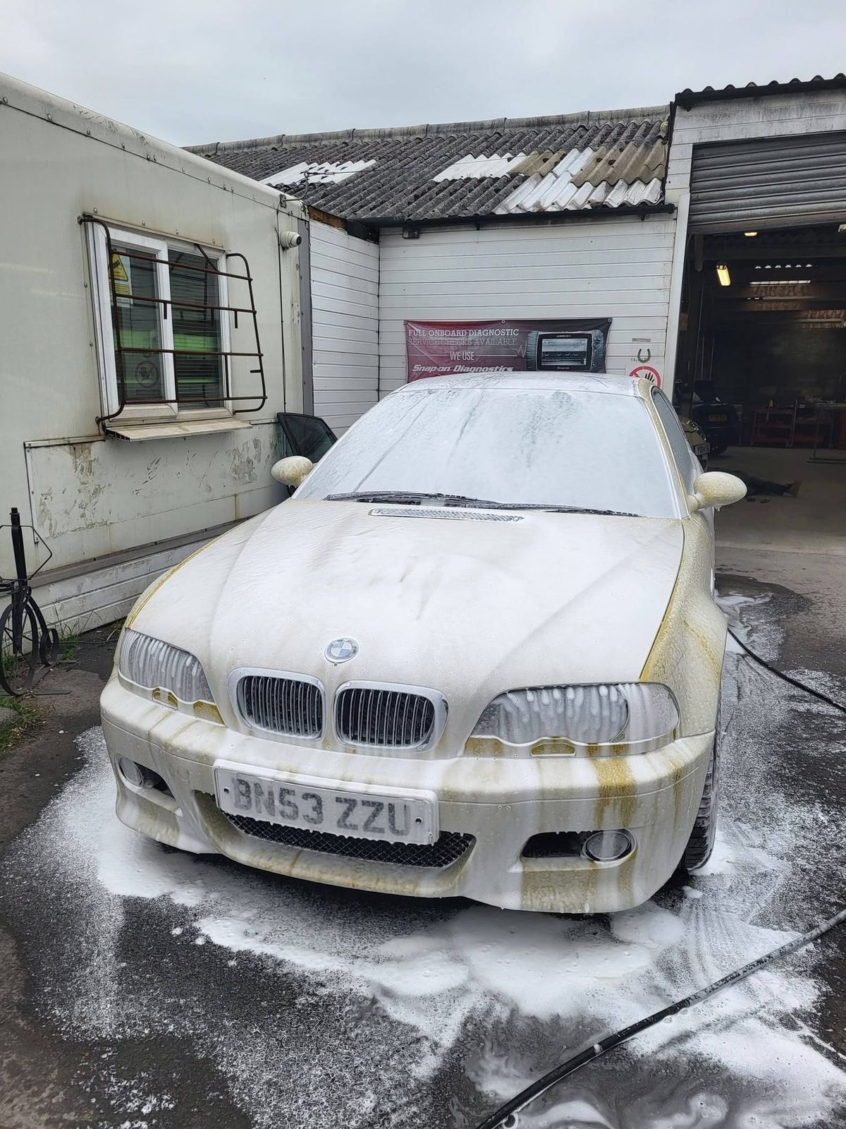 A coupe covered head to foot in thick white snow foam during the pre-wash stage